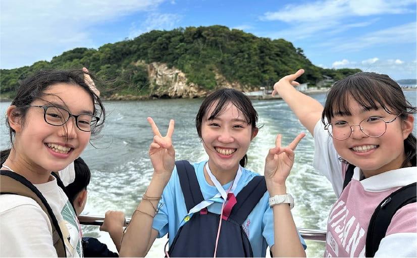 女の子三人が海で山を背景に写真撮影