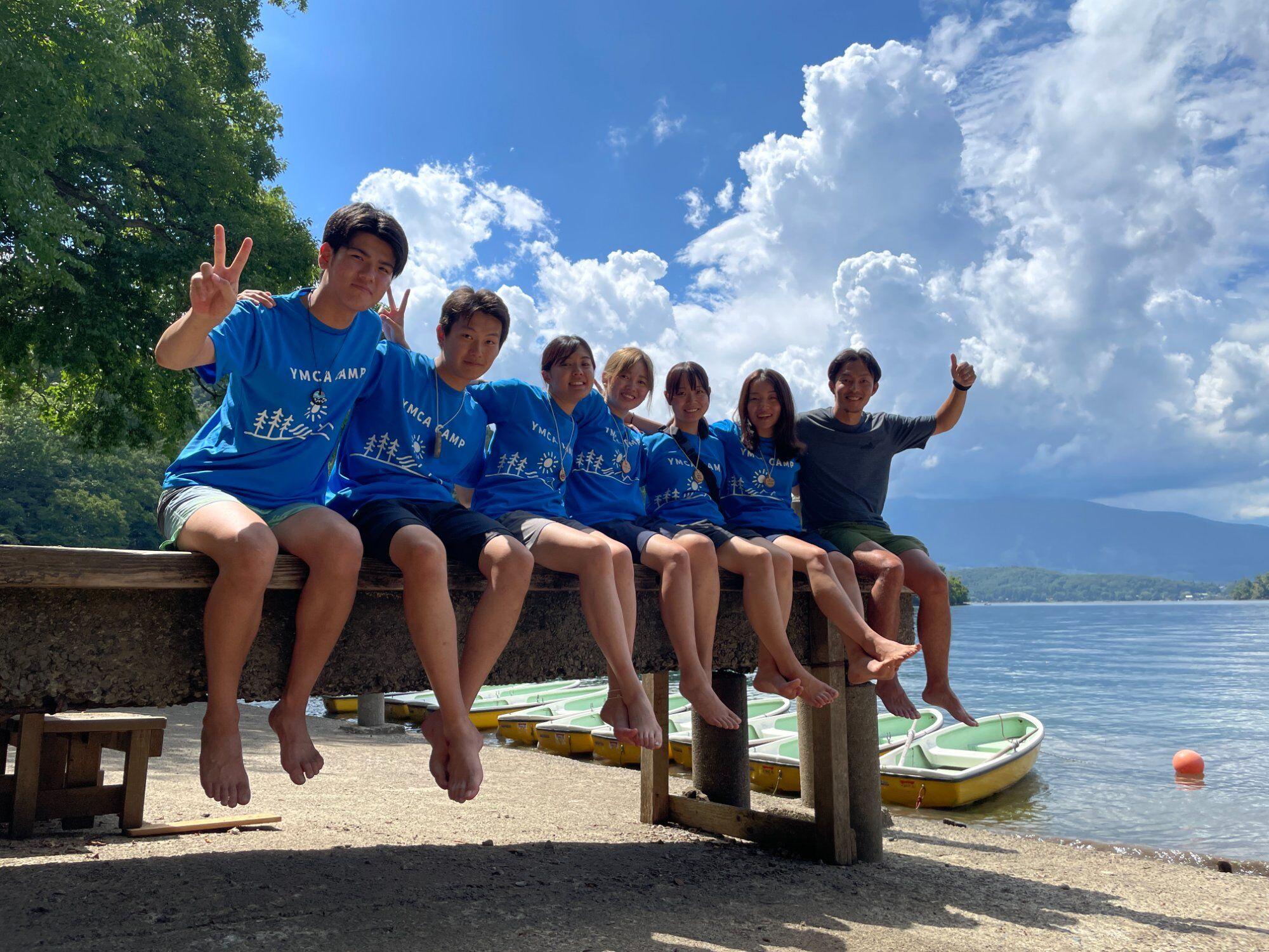 湖畔に座るYMCAキャンプのユースボランティアたち
